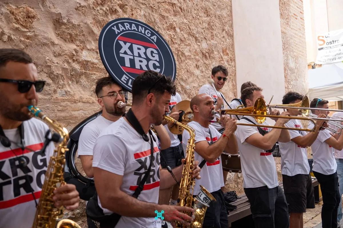 Saxofones y trombones de Xaranga El Truc tocando junto a una pared de piedra