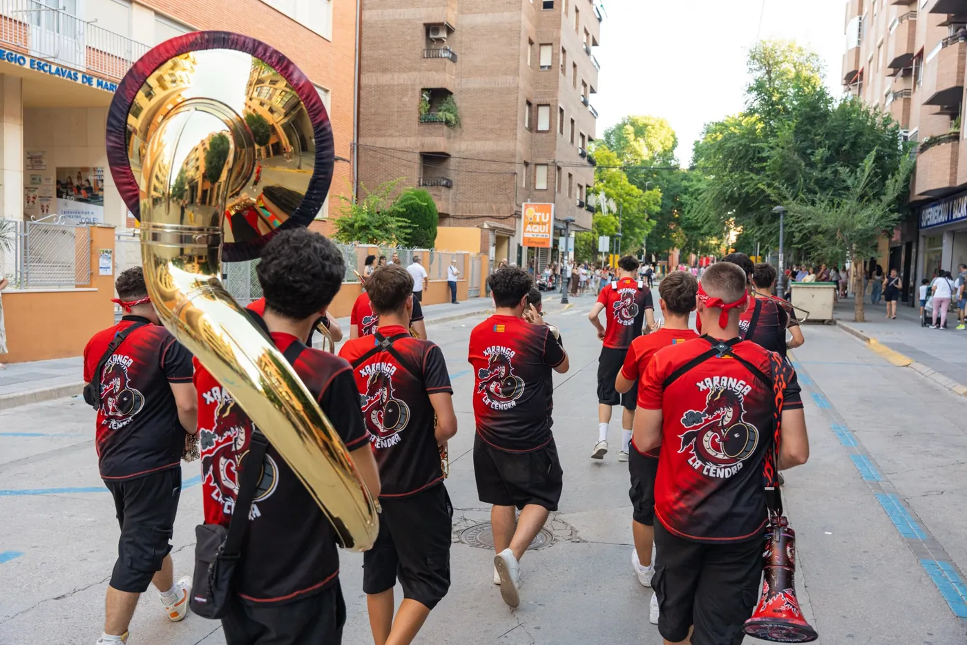 Xaranga La Cendra desfilando por la calle con camisetas rojas y negras y una tuba